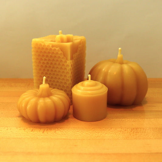Yellow candles made of pure beeswax in various shapes and patterns including a bee hive, a large and small pumpkin, and a votive.
