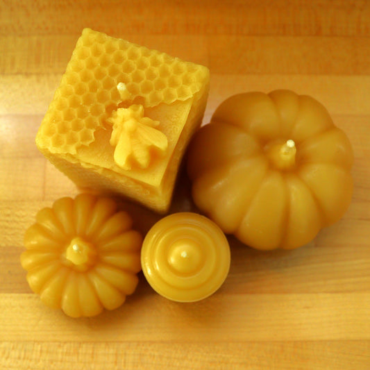 Yellow candles made of pure beeswax in various shapes and patterns including a bee hive, a large and small pumpkin, and a votive.